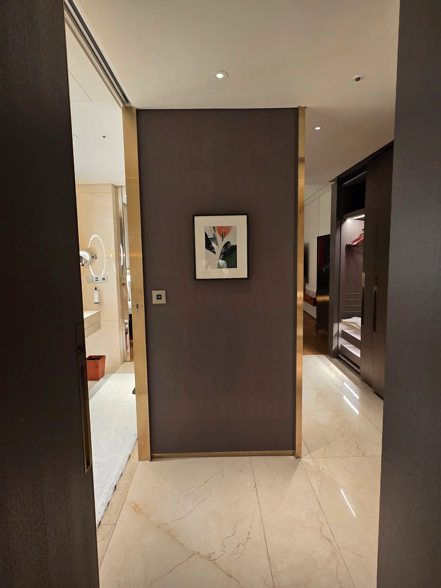 갈색 벽면에 액자가 걸린 호텔 객실 입구, 욕실과 침실로 이어지는 복도