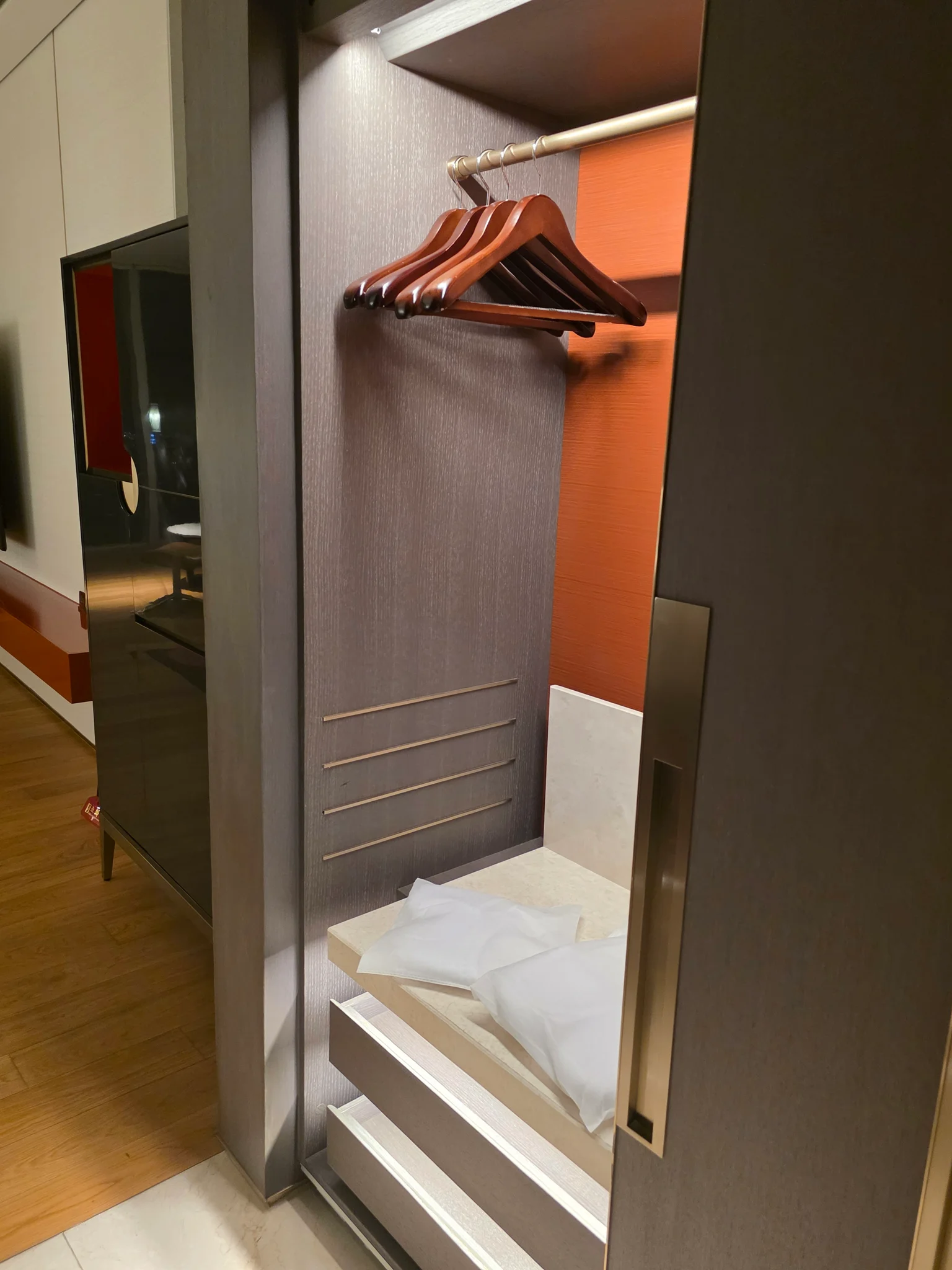 회색 톤의 개방형 옷장에 나무 행거와 흰 수건이 정리된 호텔 객실 내부