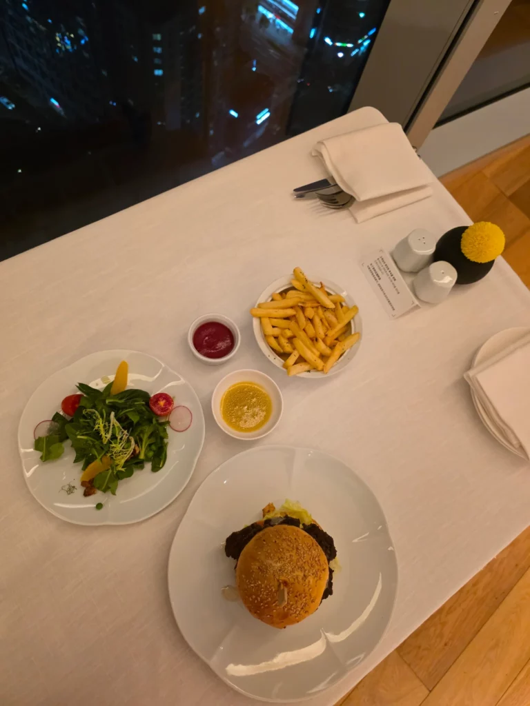 야경이 보이는 레스토랑 테이블 위 버거와 샐러드, 감자튀김 세트