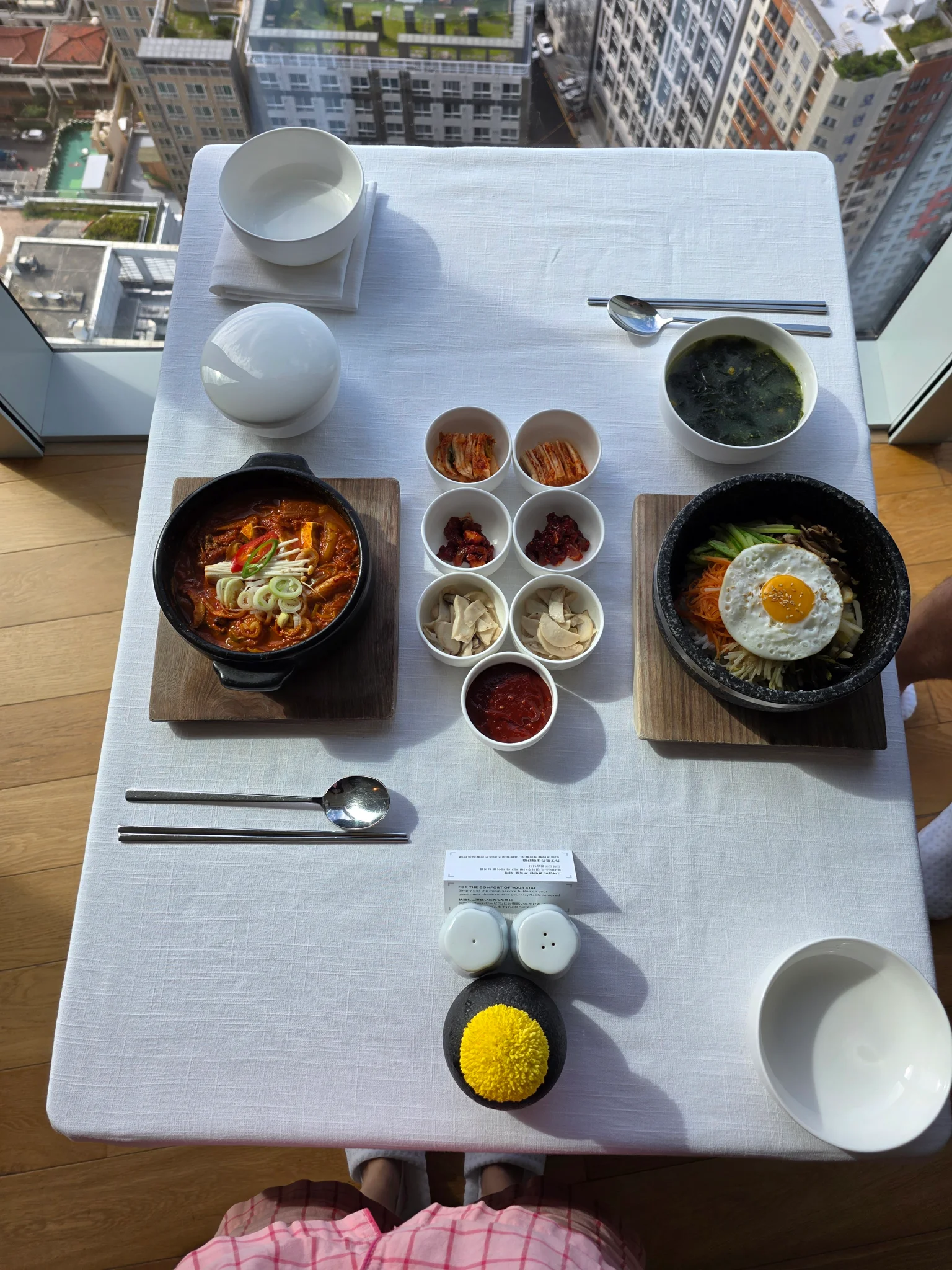 고층 빌딩 뷰가 보이는 창가 테이블에 차려진 돌솥비빔밥 2인 세트
