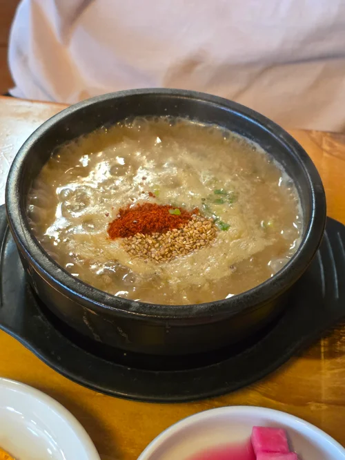 검은 돌솥에 담긴 뜨거운 사골 곰탕, 고춧가루와 깨 고명