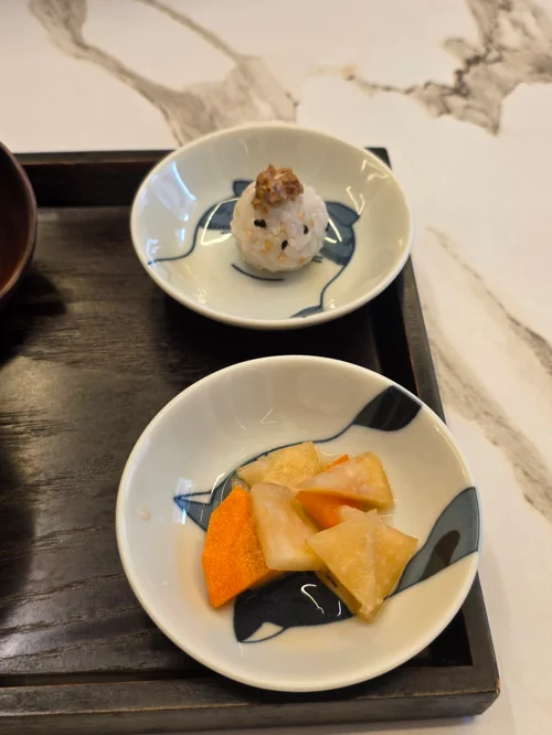 검은 트레이 위 두 접시에 담긴 주먹밥과 과일 조각