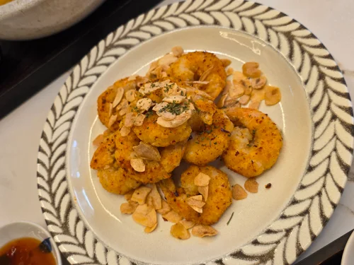 마늘칩과 허브를 얹은 황금빛 새우 튀김이 잎 문양 접시에 담긴 모습