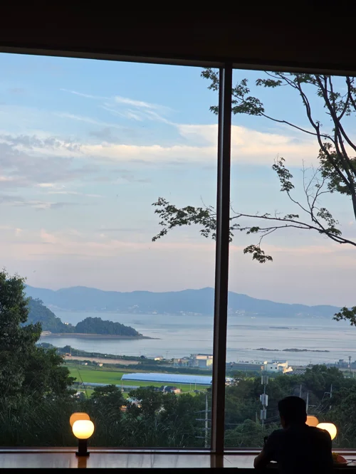 창가에 앉은 사람이 호수와 산이 보이는 석양 풍경을 바라보는 모습