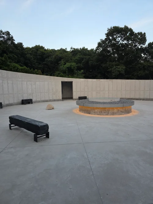 콘크리트 벽과 중앙 원형 돌 구조물이 있는 미니멀한 야외 명상 공간