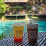터키색 수영장이 보이는 야외 테라스에 놓인 NO.39 브랜드 음료 두 잔