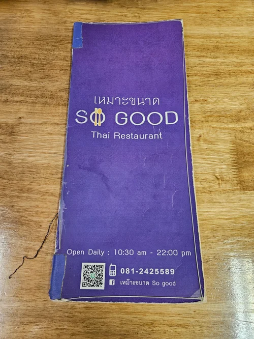 보라색 'SO GOOD Thai Restaurant' 메뉴판이 나무 테이블 위에 놓여있는 모습