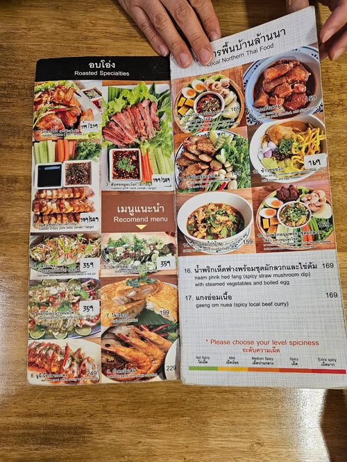 태국어와 영어로 작성된 태국 레스토랑 메뉴판이 나무 테이블 위에 펼쳐진 모습