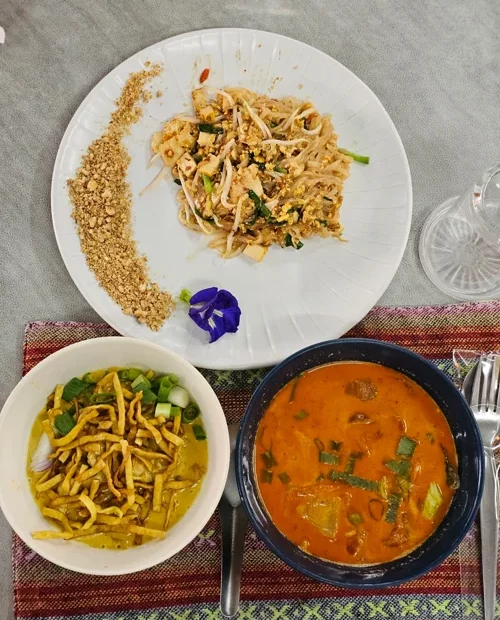 흰 접시의 팟타이와 카레면, 똠얌꿍 수프가 담긴 태국 음식 세트