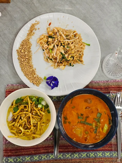 흰 접시의 팟타이와 카레면, 똠얌꿍 수프가 담긴 태국 음식 세트