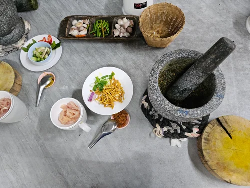 대리석 테이블 위에 돌절구와 신선한 재료들이 놓여있는 태국 요리 준비 장면