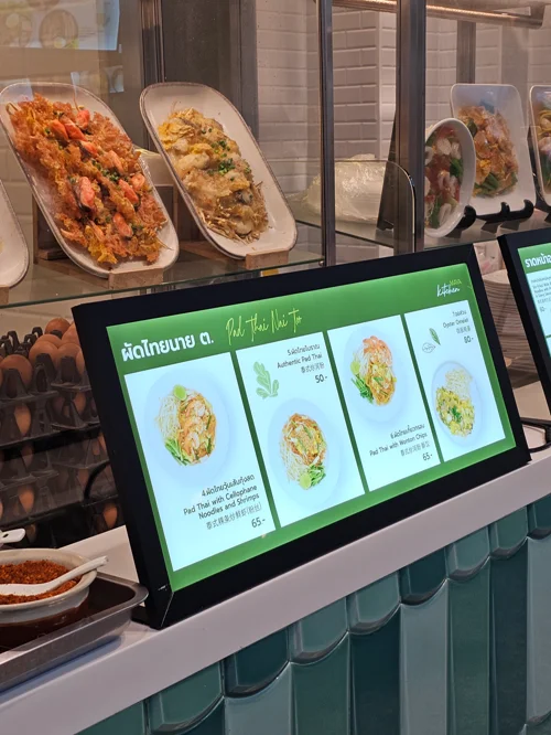 태국 음식점의 샐러드 메뉴를 보여주는 디지털 주문 화면과 배경의 해산물 요리 진열대