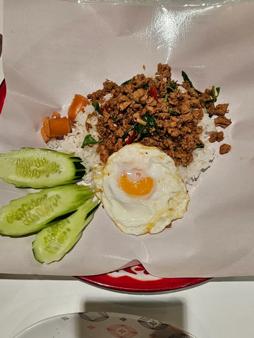 흰 쌀밥 위에 바질 다진고기볶음과 계란후라이, 오이가 담긴 태국식 볶음밥