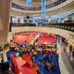 복층 쇼핑몰 중앙에 빨간색 파란색 카펫과 풍선 장식으로 꾸며진 크리스마스 이벤트 공간