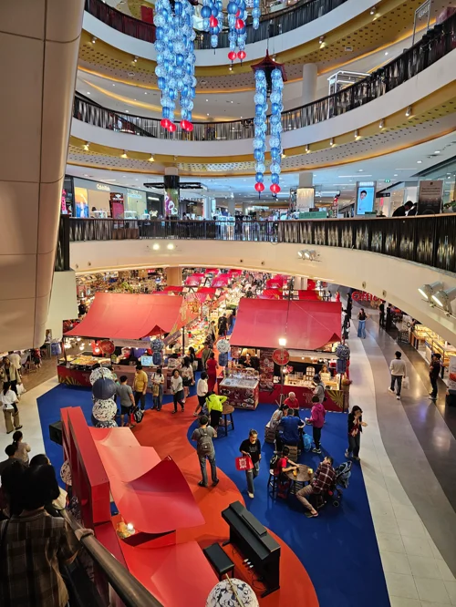 복층 쇼핑몰 중앙에 빨간색 파란색 카펫과 풍선 장식으로 꾸며진 크리스마스 이벤트 공간