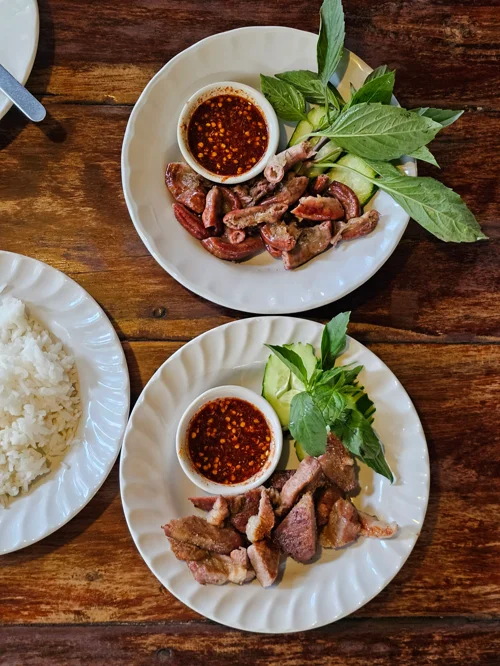 나무 테이블에 놓인 구운 고기 두 접시와 매콤한 소스, 신선한 채소 곁들임