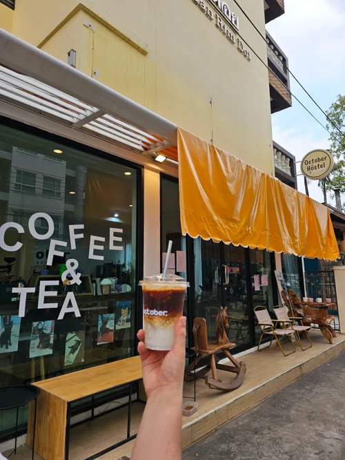 노란색 차양이 있는 카페 앞에서 아이스 음료를 든 손