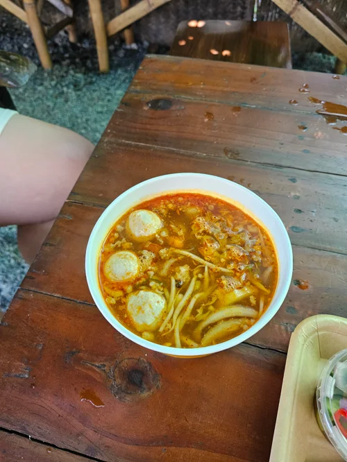 나무 테이블 위 하얀 그릇에 담긴 매운 라면과 삶은 계란 세 개