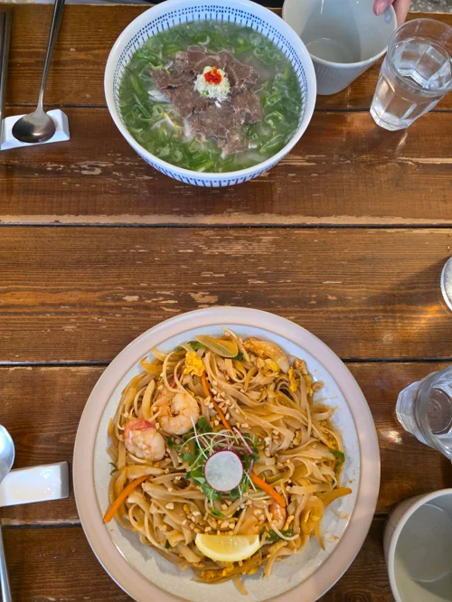 나무 테이블 위 베트남 쌀국수와 새우 팟타이가 담긴 두 그릇