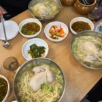 스테인리스 그릇에 담긴 칼국수와 다양한 반찬이 차려진 한식당 테이블