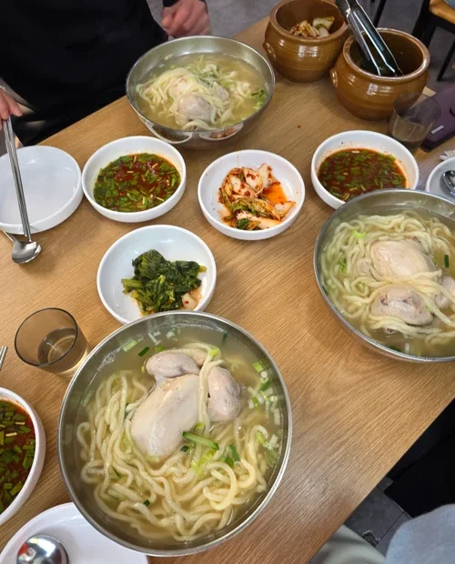 스테인리스 그릇에 담긴 칼국수와 다양한 반찬이 차려진 한식당 테이블