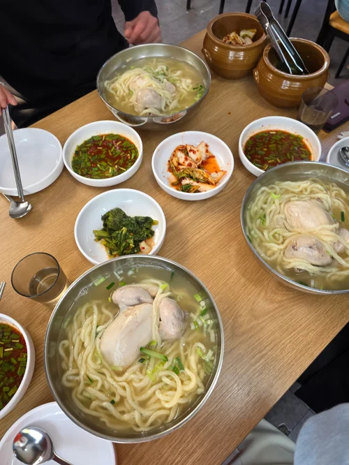 스테인리스 그릇에 담긴 칼국수와 다양한 반찬이 차려진 한식당 테이블