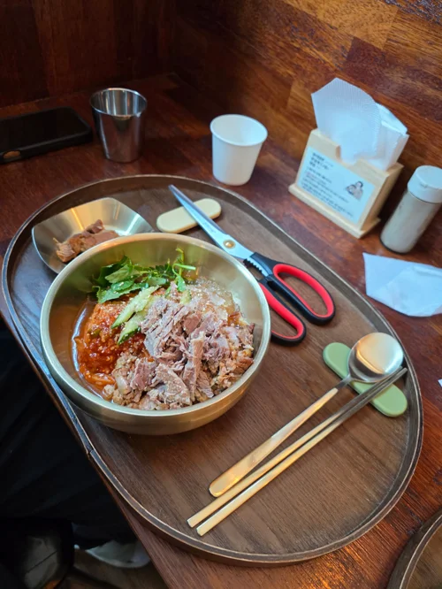 나무 쟁반 위에 담긴 고기와 채소가 들어간 한식 육수 요리