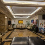 금빛 몰딩과 간접조명이 있는 천장 아래 크림색 소파가 놓인 고급 호텔 로비