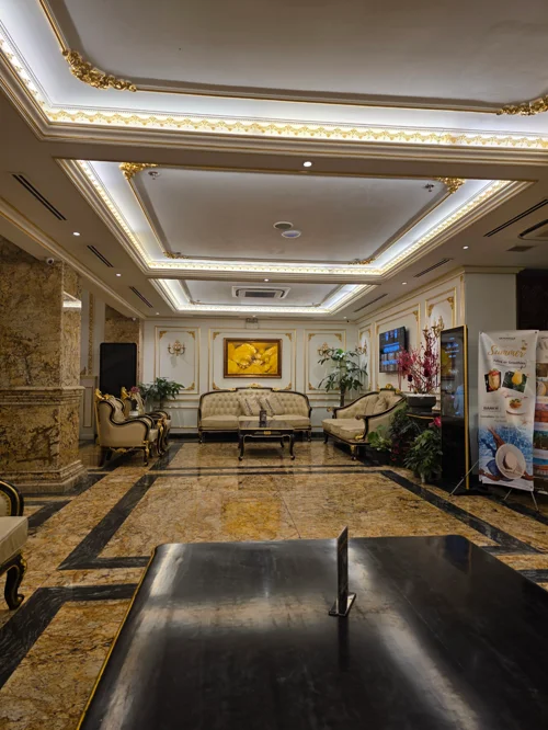 금빛 몰딩과 간접조명이 있는 천장 아래 크림색 소파가 놓인 고급 호텔 로비