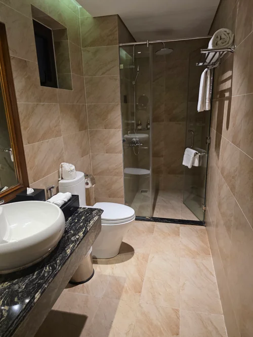 베이지 대리석으로 마감된 호텔 욕실, 유리 샤워부스와 원형 세면대