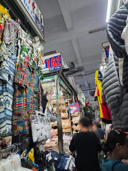 한시장 내부 통로, 양옆에 패딩과 옷가지가 진열되어 있고 사람들이 쇼핑 중