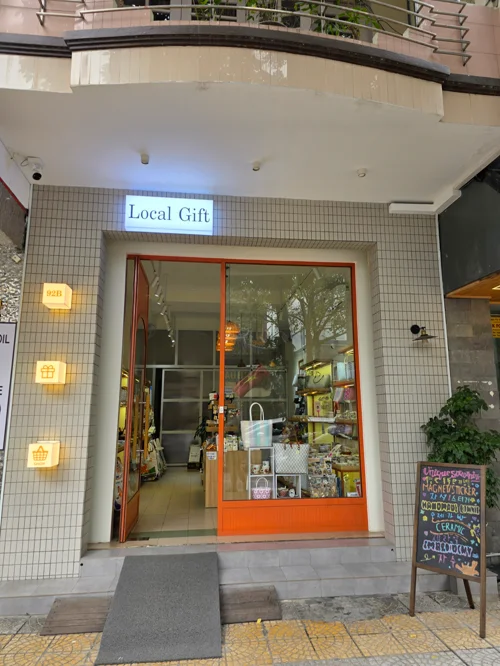 화이트 타일 외벽과 주황색 프레임 유리문이 있는 로컬 기프트샵 입구