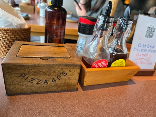 PIZZA 4 P'S 로고가 새겨진 티슈케이스와 조미료 병들이 담긴 나무 트레이