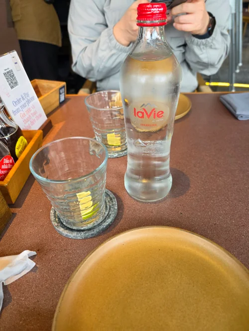 갈색 테이블 위에 놓인 라비 생수병과 물잔 두 개