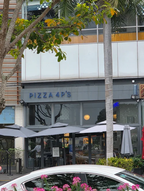 PIZZA 4P'S 간판이 있는 화이트 톤의 2층 레스토랑 외관과 야자수, 야외 테라스