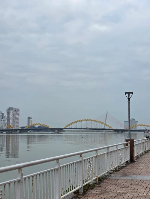 한강 위의 황금색 아치형 다리와 배경의 고층 빌딩, 전경의 산책로 난간