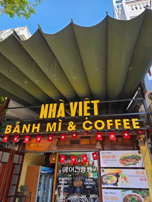 노란색 간판의 베트남 반미와 커피 전문점 외관, 올리브색 곡선 차양막 아래 메뉴판 전시