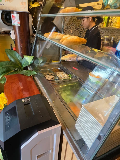 유리 진열대에 바게트빵이 놓여있고 냉장 진열대에 각종 재료가 담긴 반미 가게 조리 공간