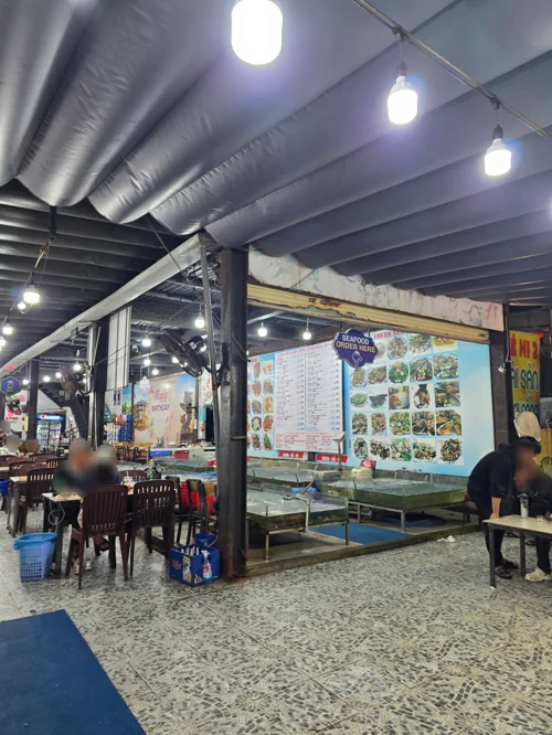 노출천장과 조명이 있는 푸드코트 내부, 메뉴판이 부착된 음식점 부스와 식탁