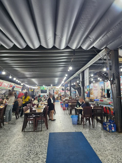 은색 덕트 천장이 있는 실내 푸드코트에서 사람들이 식사하는 모습