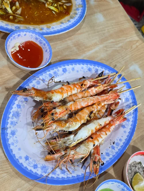 파란 접시에 담긴 꼬챙이 대하 구이 4-5마리와 칠리 소스