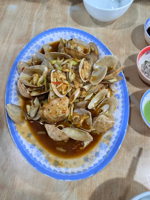 파란 접시에 담긴 바지락 두부찜, 신선한 조개와 두부가 갈색 소스에 조리되어 있음