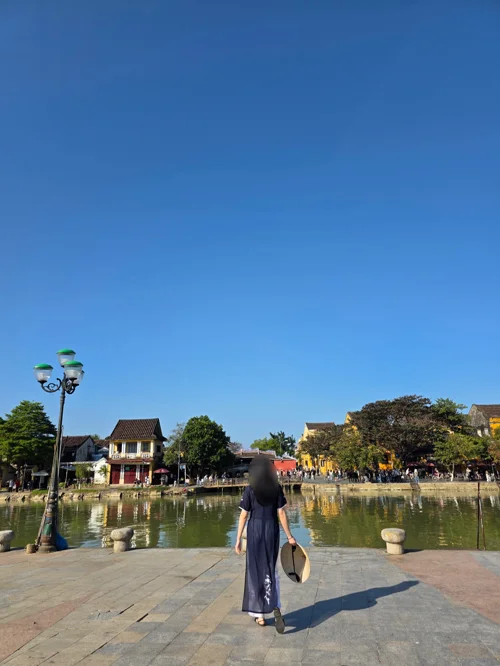 아오자이를 입고 투본강 앞에서 뒷모습을 보여주며 서 있는 여성