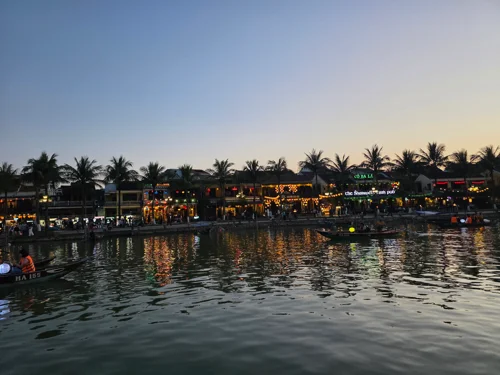 석양 무렵 강변의 전통 건물들과 야자수가 어우러진 동남아 마을 풍경