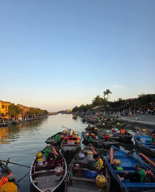 호이안 투본강에 정박한 여러 척의 전통 목선과 노란 건물들이 보이는 저녁 노을 풍경