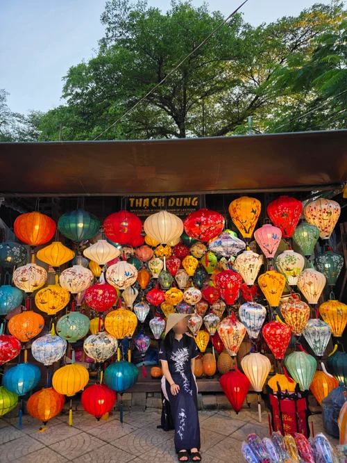 호이안 랜턴 가게 앞에서 검은 아오자이를 입은 여성과 형형색색의 전통 등불