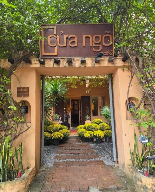 Cửa Ngõ 카페의 크림색 아치형 입구와 노란 국화가 있는 통로