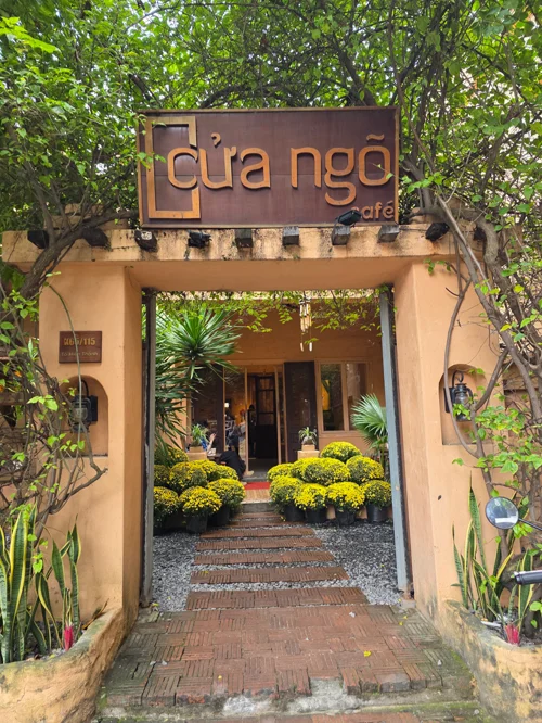 Cua Ngo 카페의 크림색 아치형 입구와 노란 국화가 있는 통로