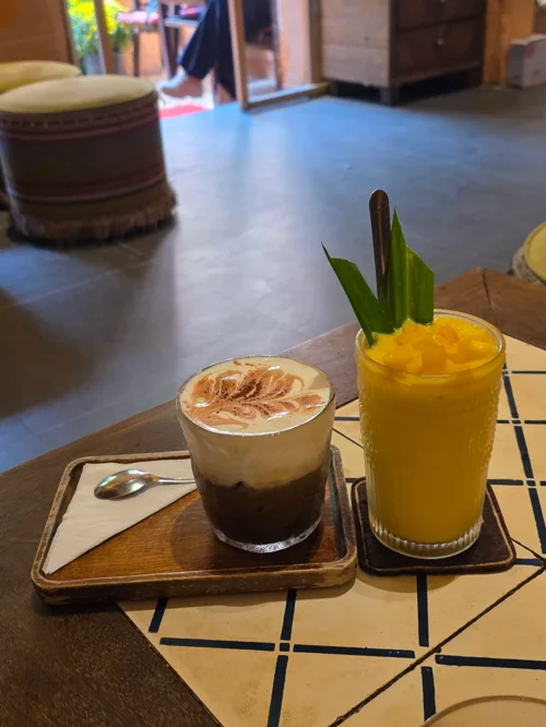 나무 트레이 위 라떼아트가 된 카페라떼와 열대잎 장식 망고음료