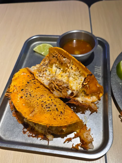 트레이에 담긴 치즈와 고기가 풍성한 멕시칸 타코 두 개와 라임, 소스